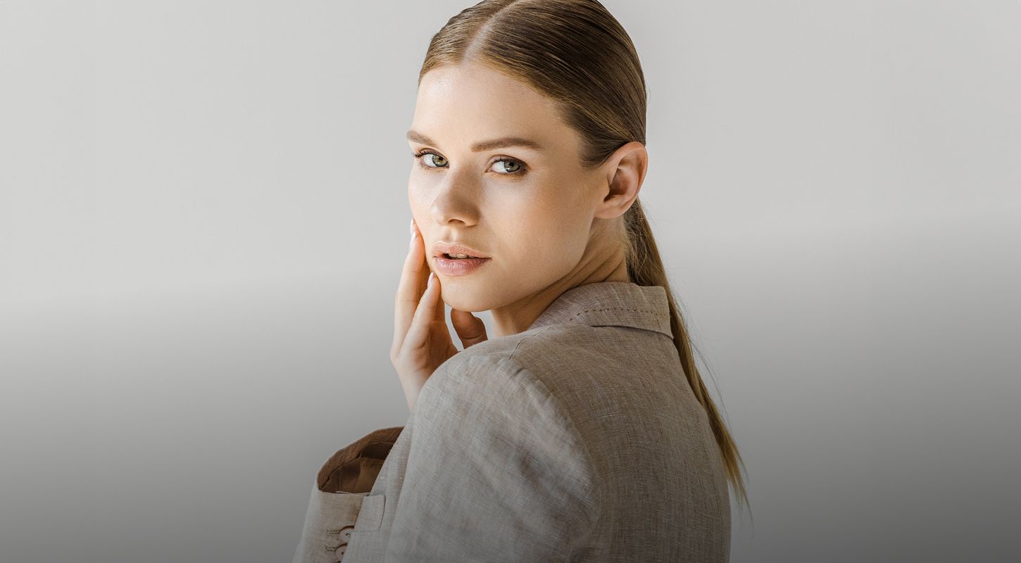 Woman with light makeup in neutral-toned outfit.