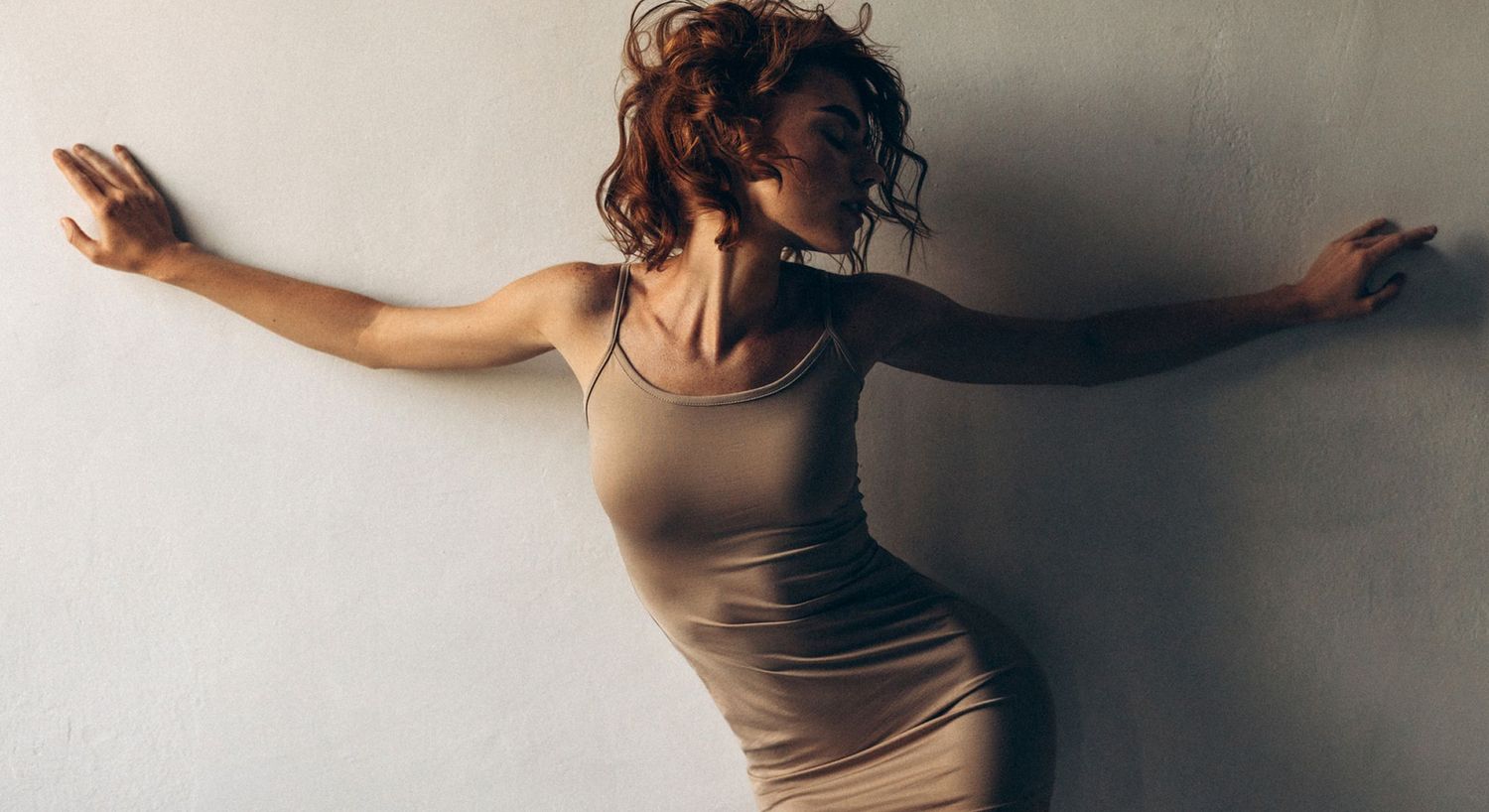 Woman in fitted dress against a wall.